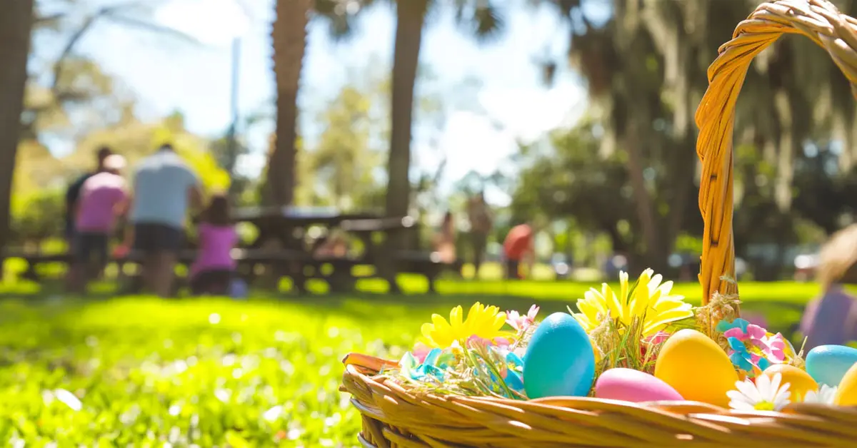 Cheerful Easter scene in a Tampa park with families in the background and a close-up of a festive Easter basket on the grass under sunny Florida skies.