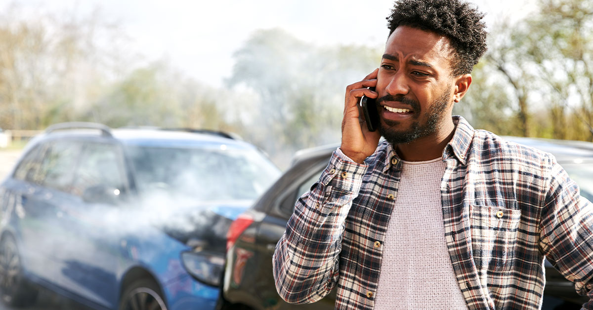 Young man standing by damaged car after traffic accident reporting incident to insurance