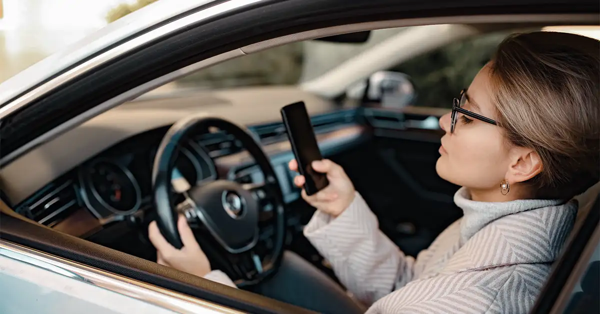 Woman sitting in car texting with her hand on the steering wheel